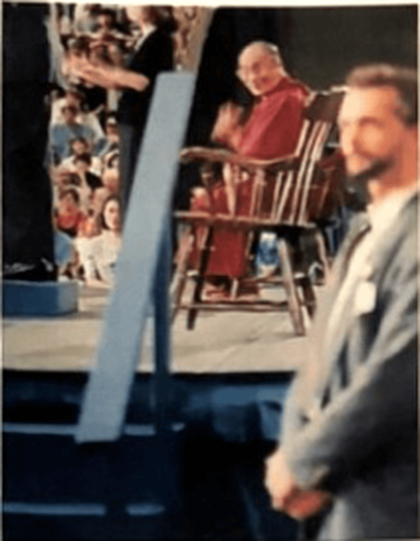 Allen Pittman standing in the foreground while the Dalai Lama sits on stage behind him